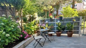 Un patio al aire libre con una mesa y sillas, rodeado de plantas en macetas y una variedad de flores.