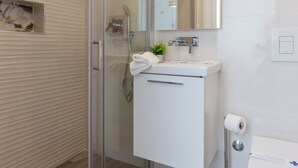 Un baño moderno con cabina de ducha de vidrio, un lavabo blanco con espejo arriba y un inodoro a la derecha.