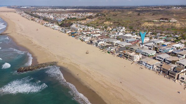 An aerial view of a coastal town with a beach, houses, and a rocky breakwater.