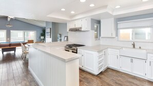 Una cocina moderna con armarios blancos, una isla central y un comedor con mesa de billar.