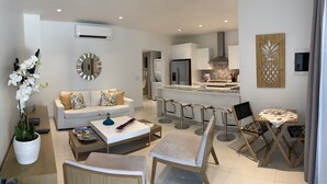 Una sala moderna con sofá, mesa de centro y sillas, un área de cocina con mesa de comedor y un espejo decorativo.