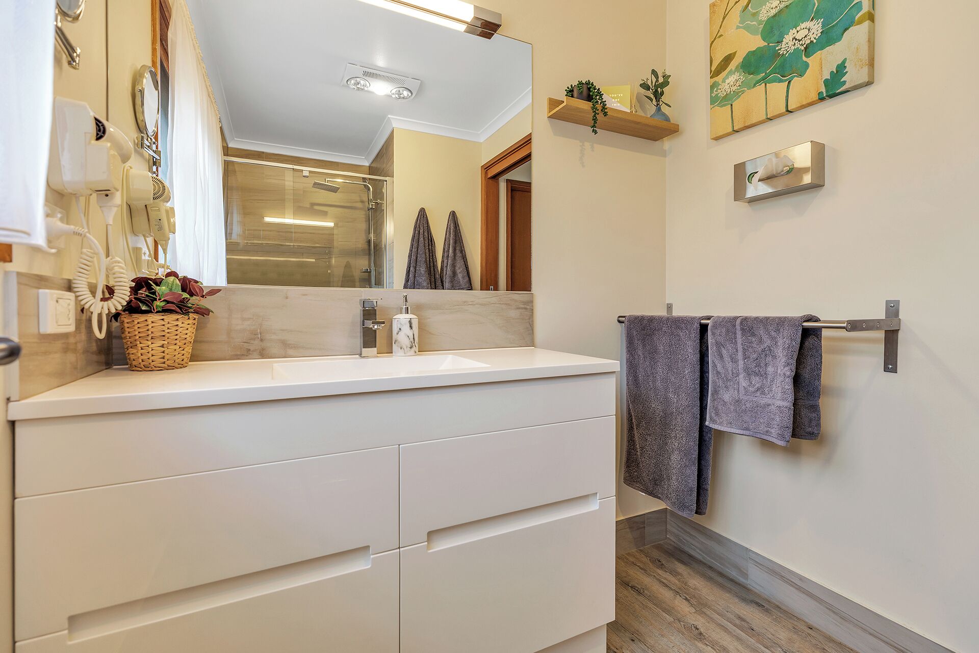 A modern bathroom with a white vanity, a glass shower enclosure, and a towel rack with two towels.