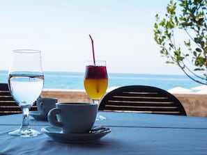 Een tafel met een glas water en een glas rode en gele drank, met uitzicht op de oceaan.