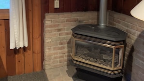 Una estufa de leña en un rincón de una habitación con paredes de madera y una chimenea de ladrillo.