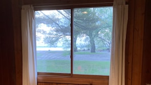 Una habitación de madera con ventana, una pequeña mesa de madera y vistas a árboles y un cuerpo de agua.