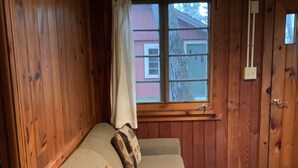 Un interior de madera con un sofá apoyado en la pared, una ventana que ofrece vistas a un edificio y una puerta.