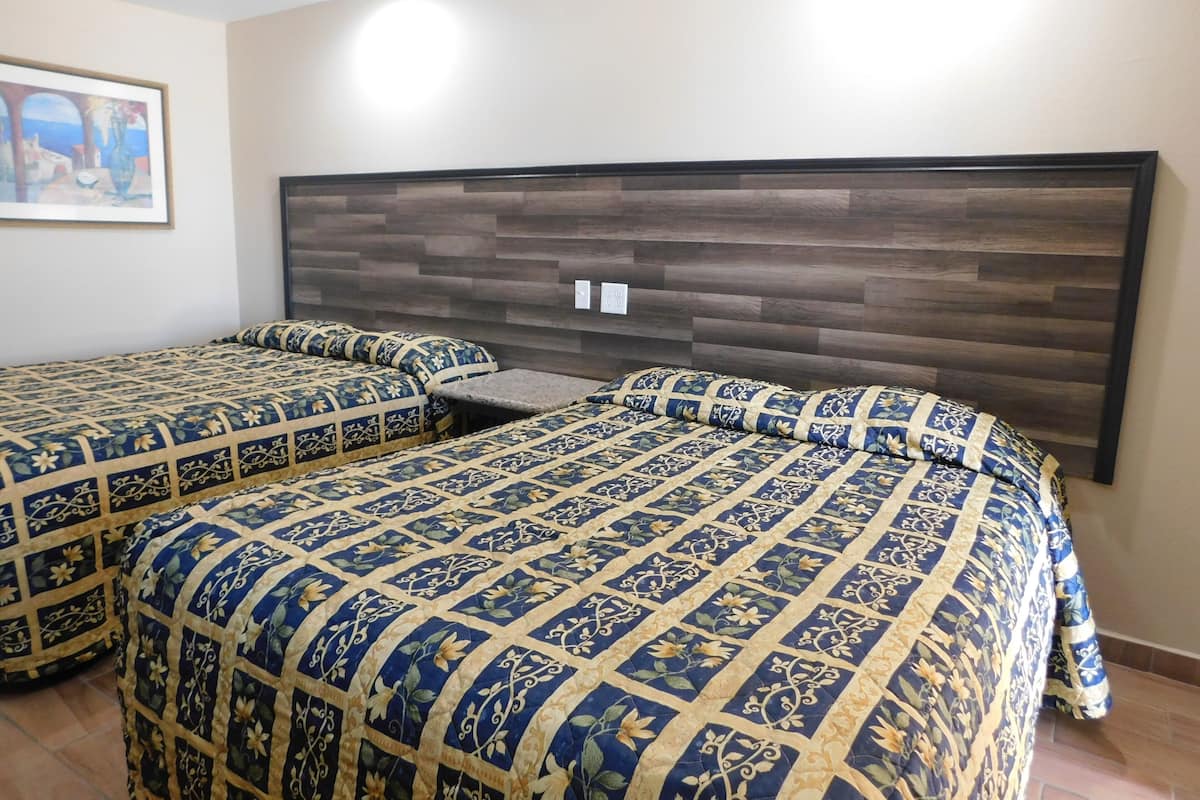 A hotel room with two beds, each with a patterned bedspread and matching pillows. The headboard is made of dark wood panels.