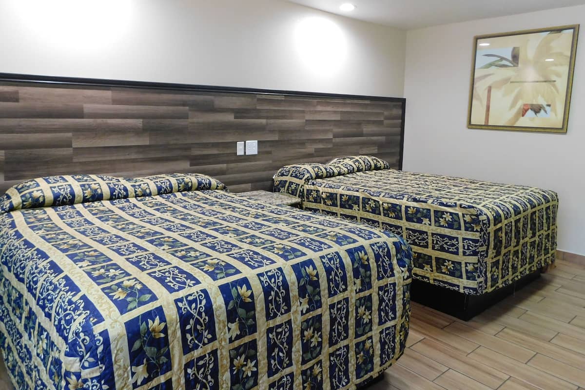 A hotel room with two beds, each with a floral-patterned bedspread, a wooden headboard, and a framed picture on the wall.