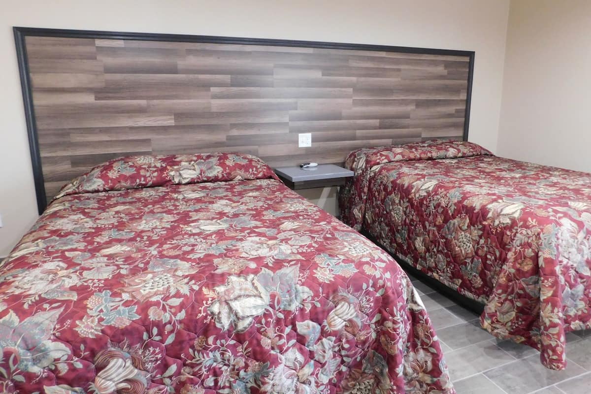 A hotel room with two beds, a wooden headboard, and a small bedside table.