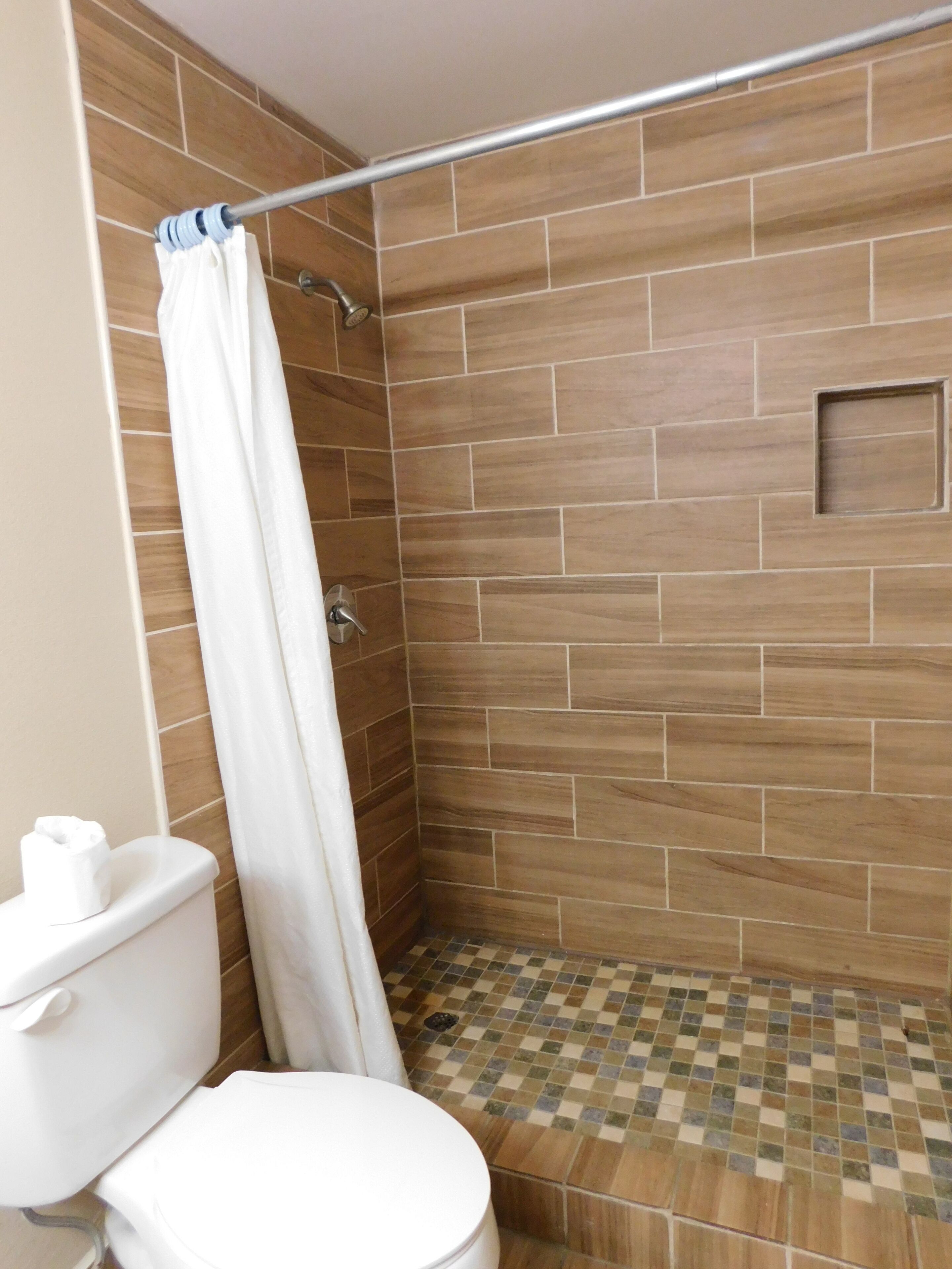 A shower area with a tiled floor, a shower curtain, and a toilet.
