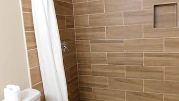 A shower area with a tiled floor, a shower curtain, and a toilet.