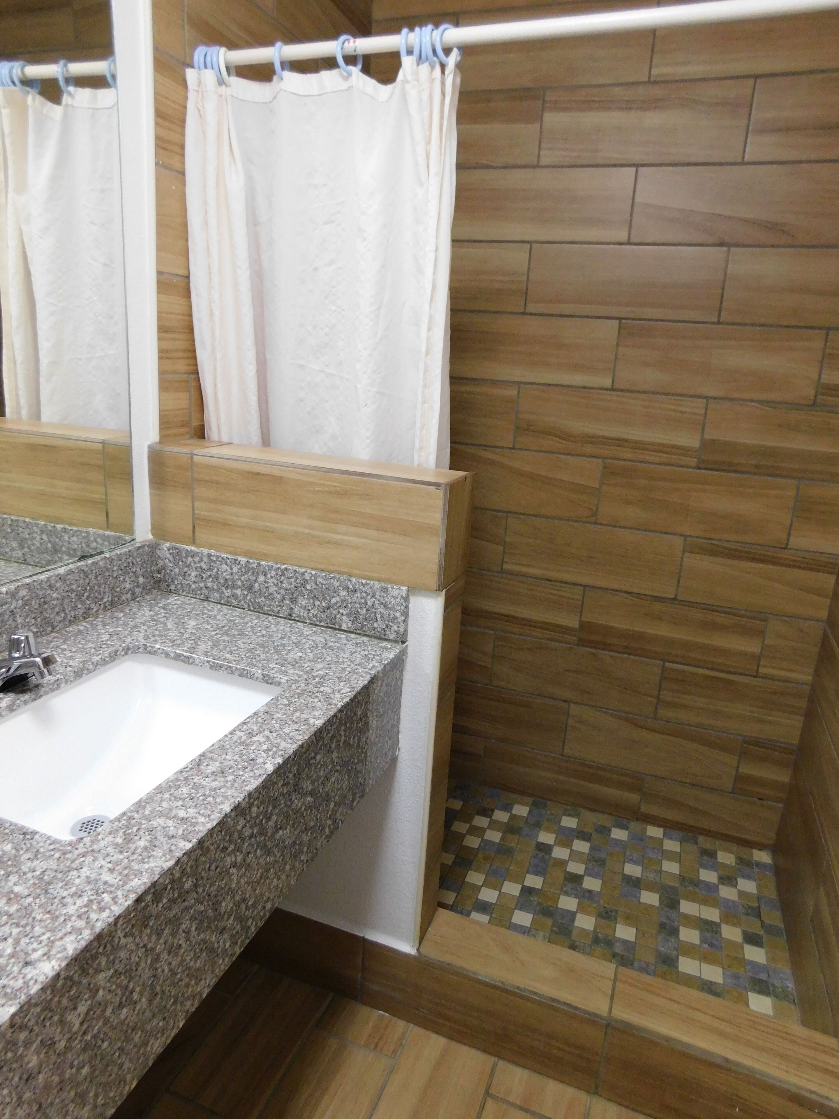 A bathroom with a granite sink, a shower with a checkered floor, and wooden wall tiles.