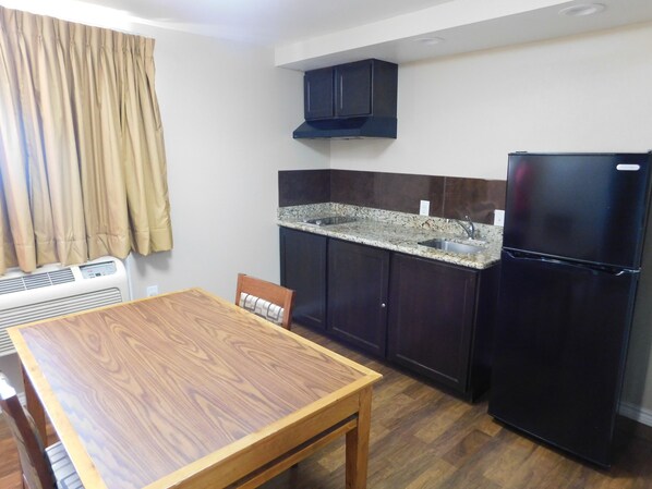 Una cocina compacta con armarios oscuros, encimera de granito, refrigerador negro y una mesa de comedor con una silla.