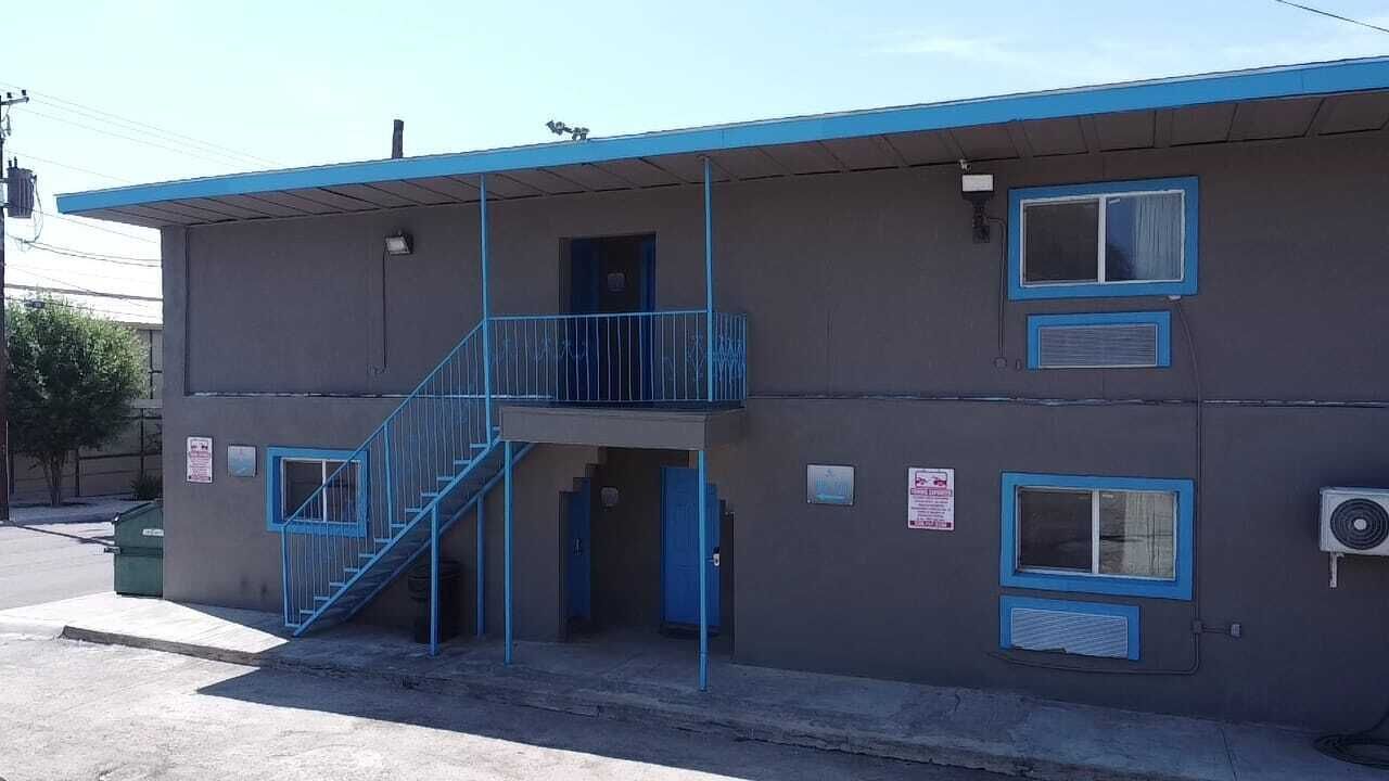 Un motel de dos pisos con fachada azul, una escalera central y un pequeño balcón en el piso superior.