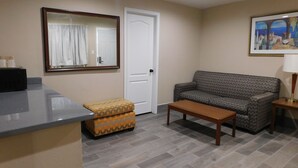 Un salon comprenant un canapé, une table basse, un pouf à motifs, un miroir et une porte.