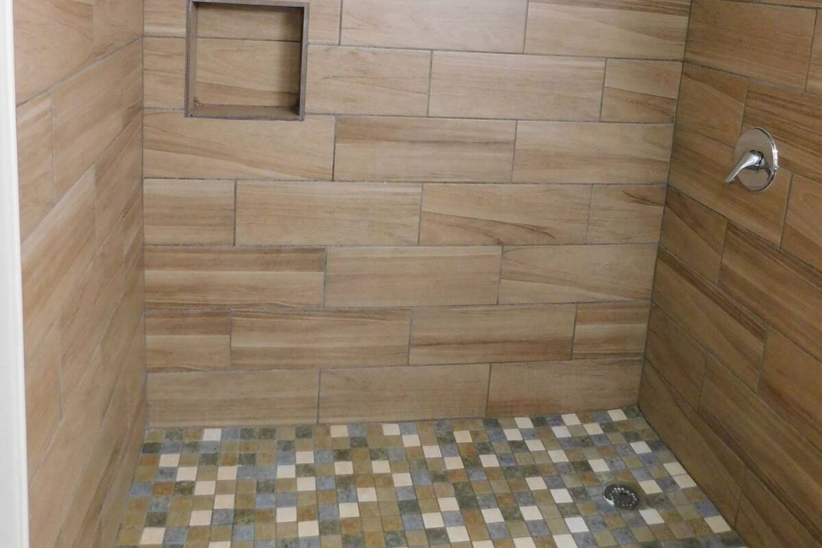A shower with a tiled floor and a small square tile inset on the wall.