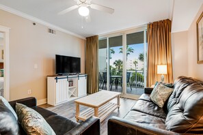 Relax in this stylish living room with a leather sofa, flat-screen TV, and sliding glass door leading to an outdoor area with a view.