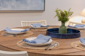 A wooden dining table with plates, cutlery, and a blue decorative bowl. - Stunning Gulf Front Three Bedroom Sanibel Condo (Sanibel)