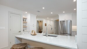 Una cocina moderna con armarios blancos, un refrigerador de acero inoxidable, una encimera de mármol y taburetes de madera.