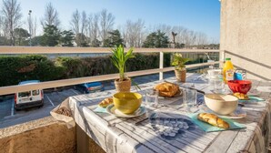 A balcony with a table set for breakfast, including croissants, bowls, and glasses, overlooking a parking area and trees. - Bastide De L'Olivier by Interhome (Le Grau du Roi)