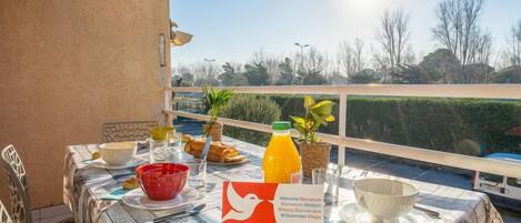 Una mesa al aire libre con alimentos para el desayuno, una botella de jugo de naranja y un cartel de bienvenida.