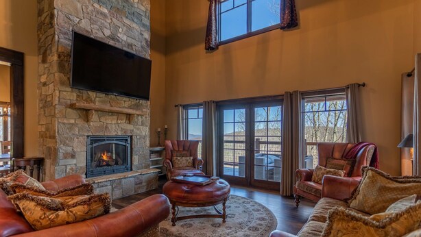 A spacious living room with a stone fireplace, leather sofas, and a large TV mounted on the wall.