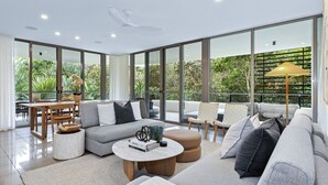 Ein modernes Wohnzimmer mit einer großen Glaswand, einem Sofa, einem Couchtisch und einem Essbereich mit Tisch und Stühlen.