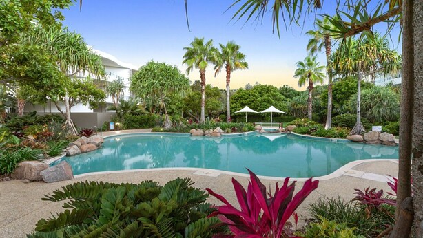 Ein Pool, umgeben von tropischen Pflanzen und Palmen, mit einem weißen Gebäude im Hintergrund.