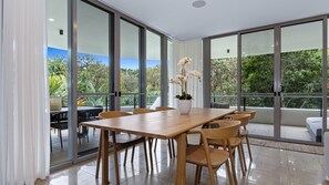 Un espace repas moderne avec une table et des chaises en bois, de grandes portes-fenêtres coulissantes et une orchidée en pot posée sur la table.