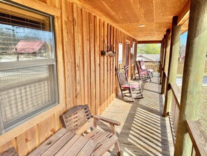 A wooden porch with benches and chairs, large windows, and a view of the outside. - Driftwood Cabin #303 (Mountain View)