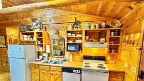 Una cocina compacta con armarios de madera, un refrigerador, un lavavajillas, una estufa y diversos utensilios y electrodomésticos de cocina.