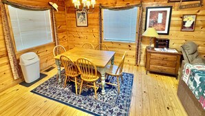 Un interior de cabaña acogedor con una mesa de comedor de madera, cuatro sillas, una araña y una mesita auxiliar con lámpara.