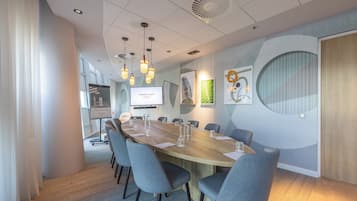 A conference room with a long table, chairs, a projector screen, and wall art.
