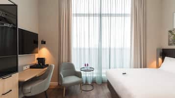 Habitación de hotel con cama, escritorio con cafetera, silla, pequeña mesa con botellas de agua y televisor.