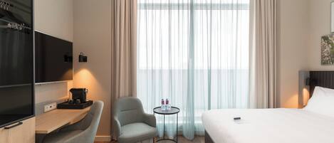 Habitación de hotel con cama, escritorio con cafetera, silla, pequeña mesa con botellas de agua y televisor.