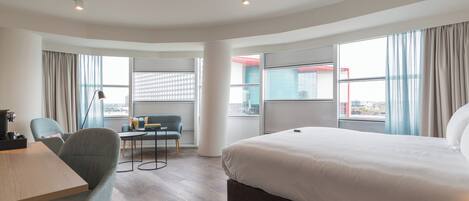 Habitación de hotel con una cama grande, un escritorio, una silla y vista a la ciudad.