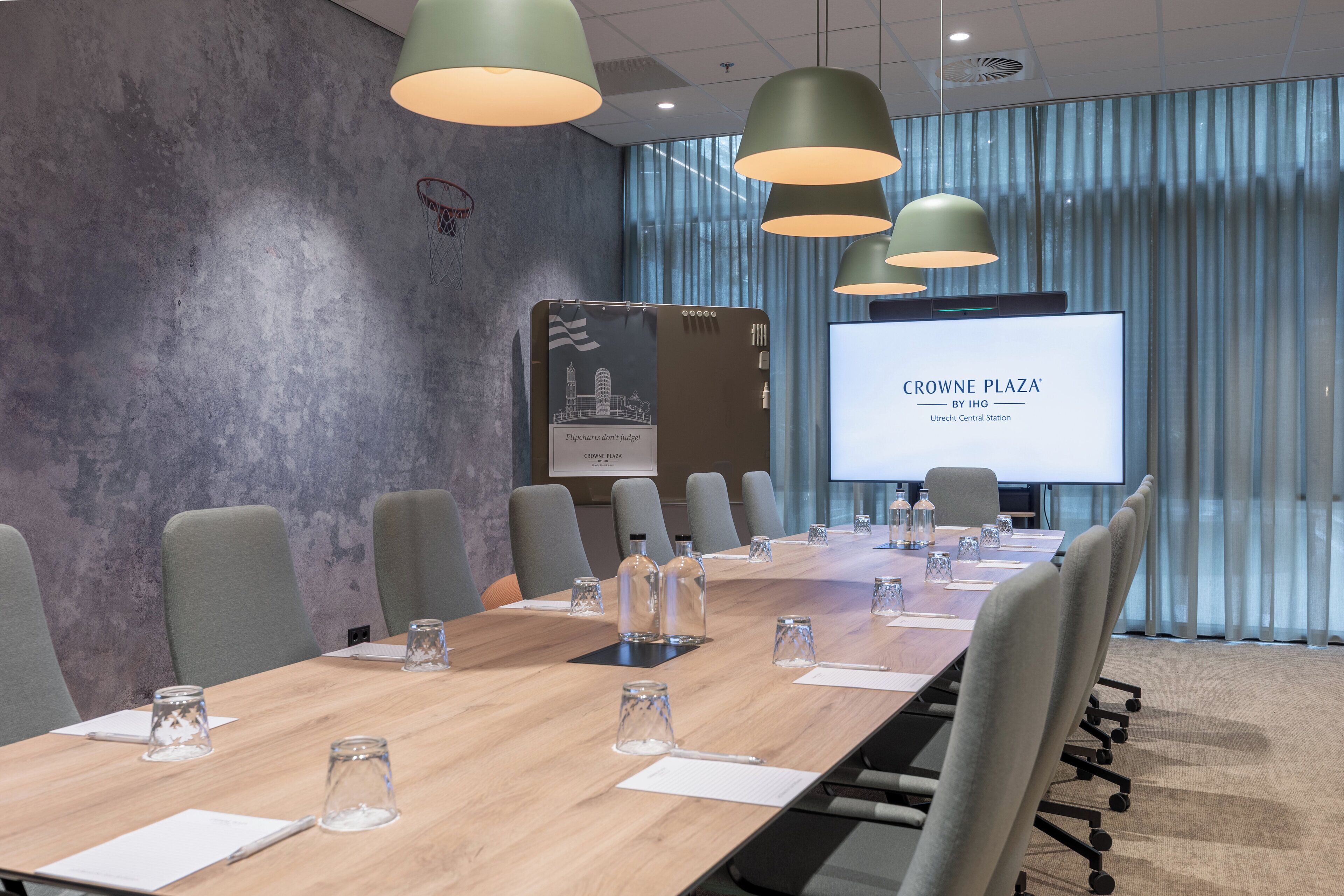 A conference room with a long table, chairs, and a screen displaying 'CROWNE PLAZA BY IHG'.