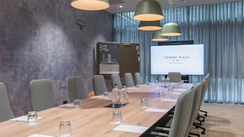 A conference room with a long table, chairs, and a screen displaying 'CROWNE PLAZA BY IHG'.