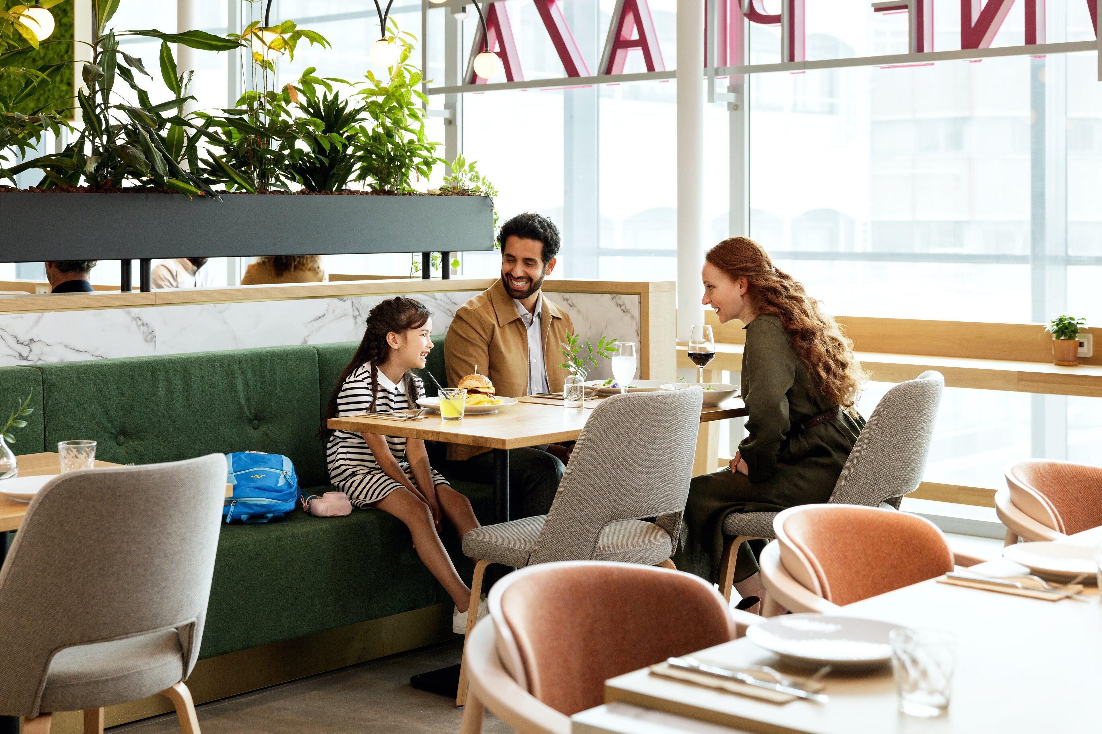 A restaurant with a green cushioned bench seating area, a wooden table, and a large window with natural light.