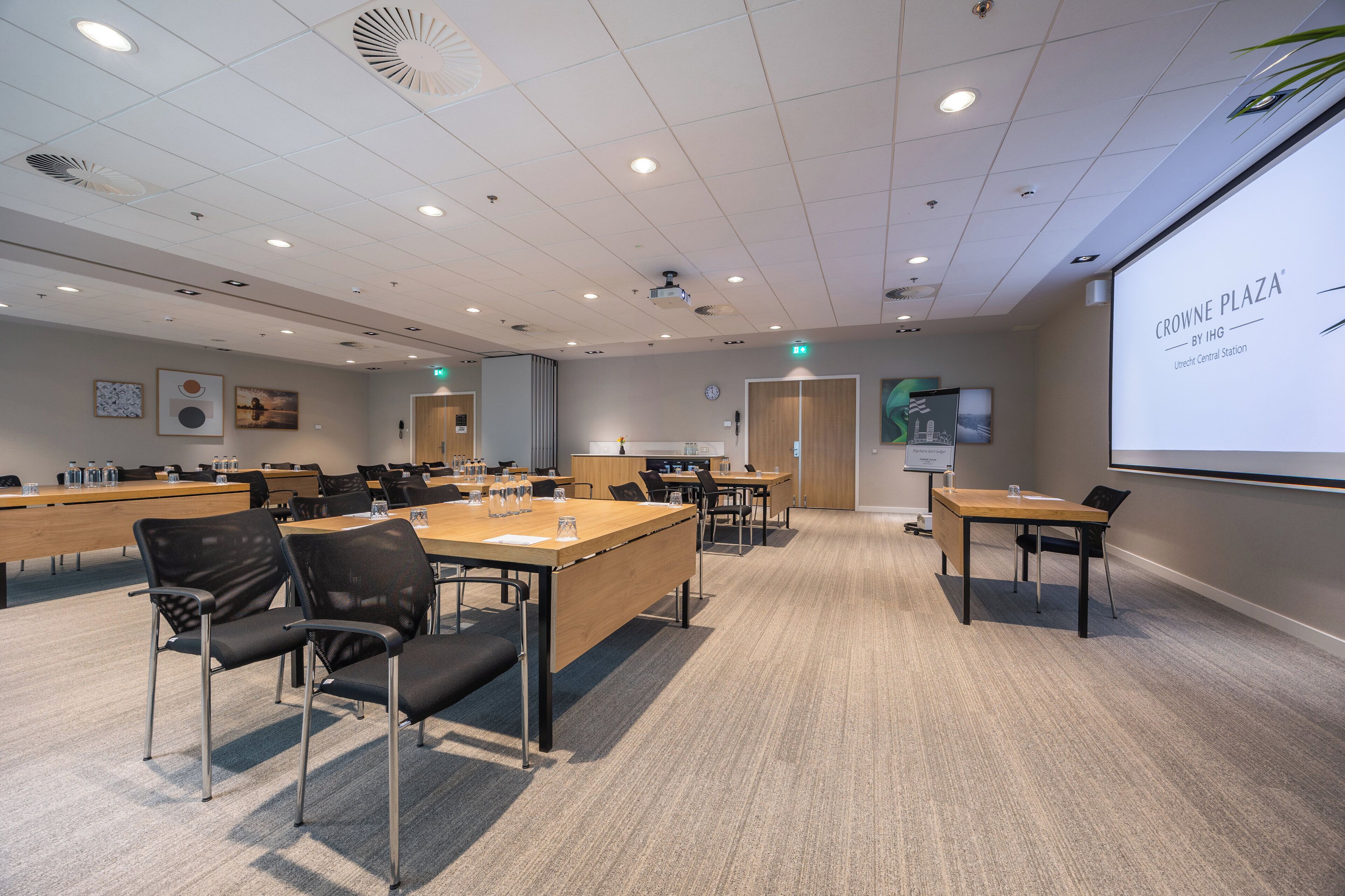 A conference room with multiple tables and chairs, a projector screen, and a clock on the wall.