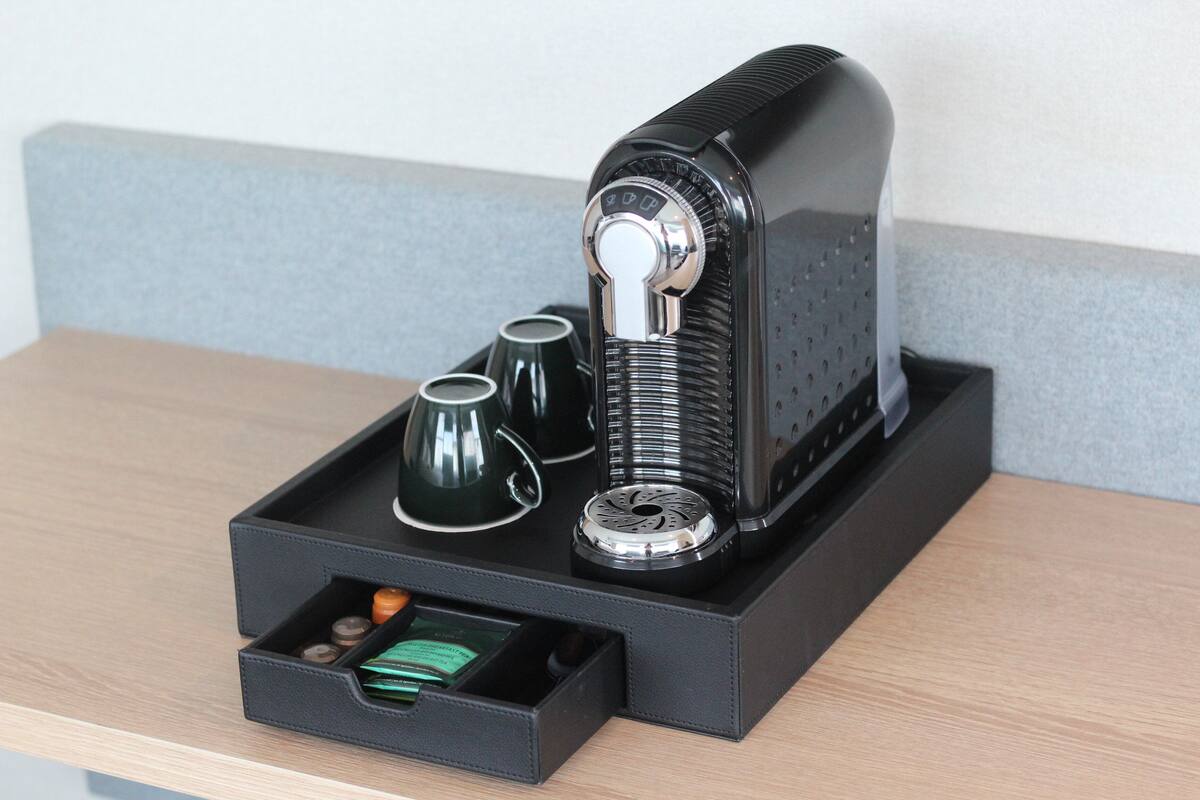 Una cafetera con un recipiente para líquidos, un cajón con cápsulas de café y dos tazas sobre una mesa de madera.