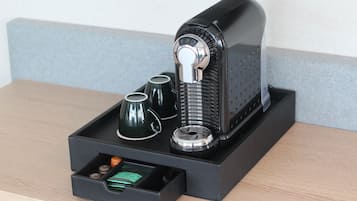 A coffee machine with a drip tray, a drawer with coffee pods, and two cups on a wooden table.