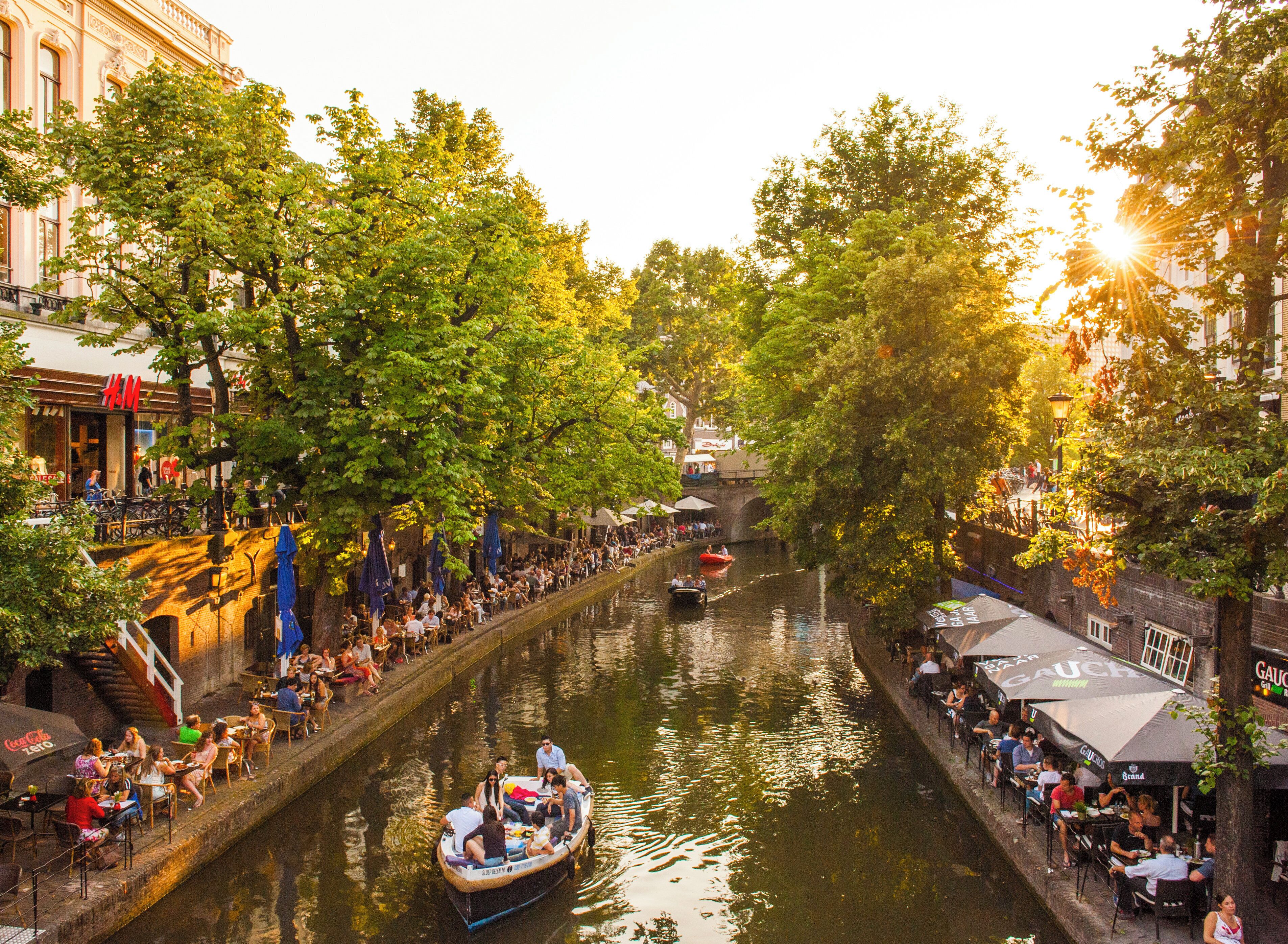 Een waterkantpromenade met terrasjes, een boot en gebouwen langs het water.