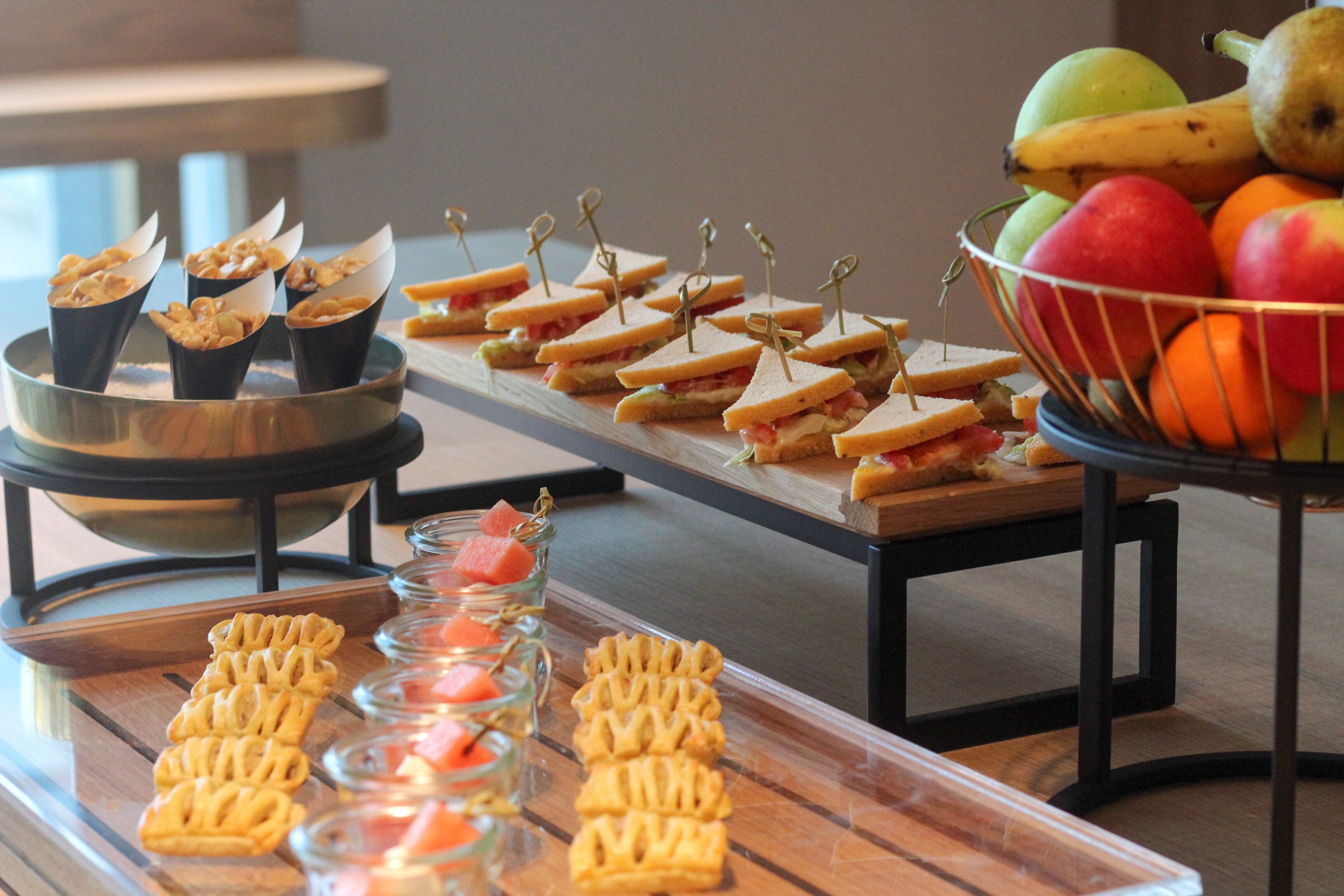 A buffet table with various food items including sandwiches, fruit, and pastries.