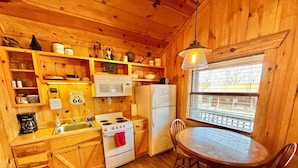 A cozy cabin-style kitchen with wooden walls, a white stove, a refrigerator, and a dining table with two chairs. - Sylamore Depot Cabin # 302 (Mountain View)