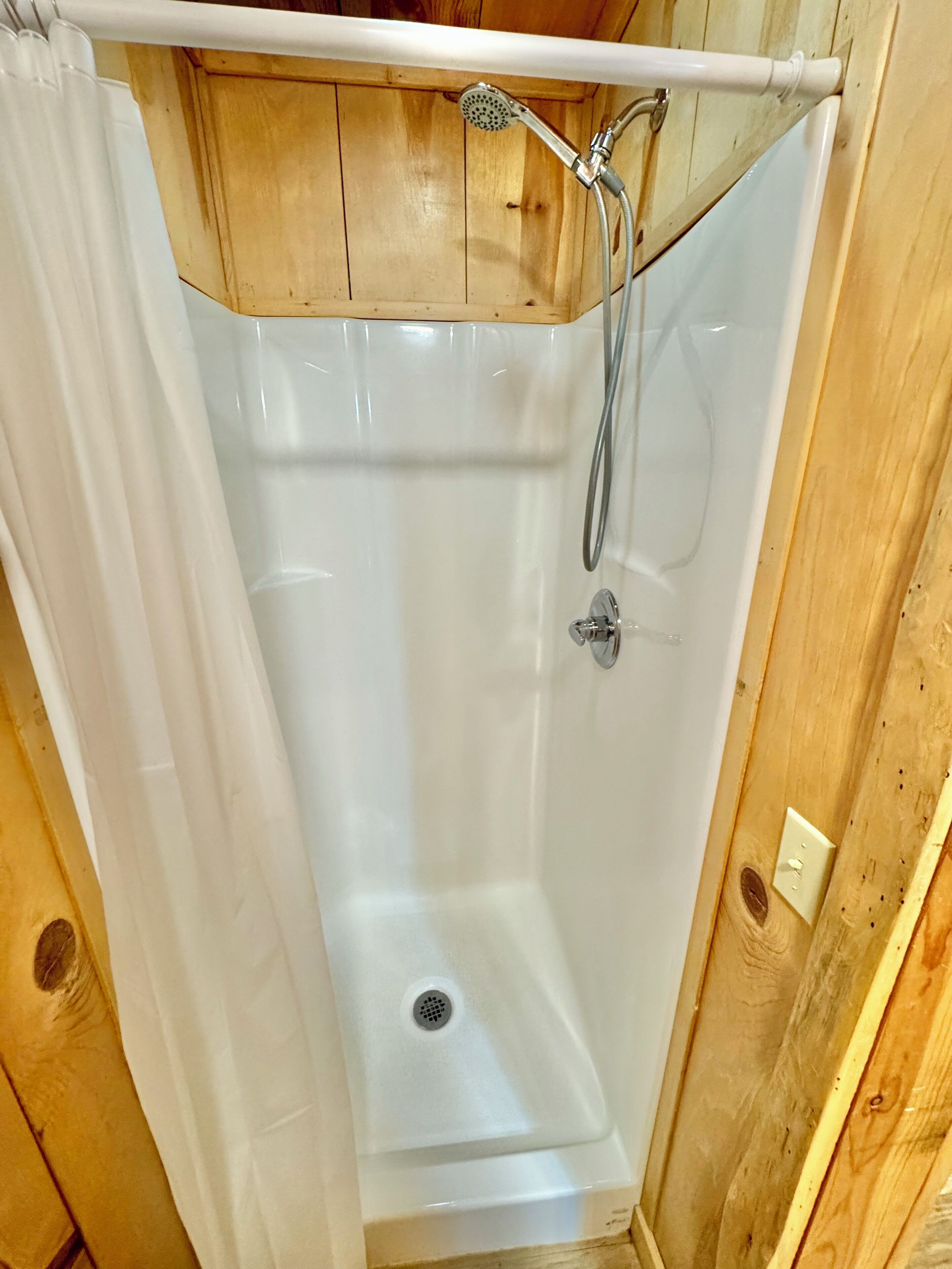 A shower with a showerhead and hose, a drain, and wooden paneling on the walls.