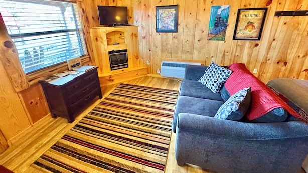 A cozy cabin interior with a fireplace, a sofa, a TV, and wooden walls. - Sylamore Depot Cabin # 302 (Mountain View)