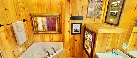 A wooden cabin bathroom with a bathtub, a sink, and framed pictures on the walls.