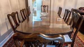 Une table ronde en verre, entourée de chaises en bois, se trouve dans une pièce dont le sol est recouvert d’un tapis à motifs.