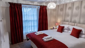 Une chambre d’hôtel avec un grand lit, des rideaux rouges, un lustre et une table de chevet avec une lampe.